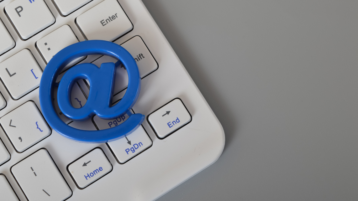 A white computer keyboard and blue email (@) symbol