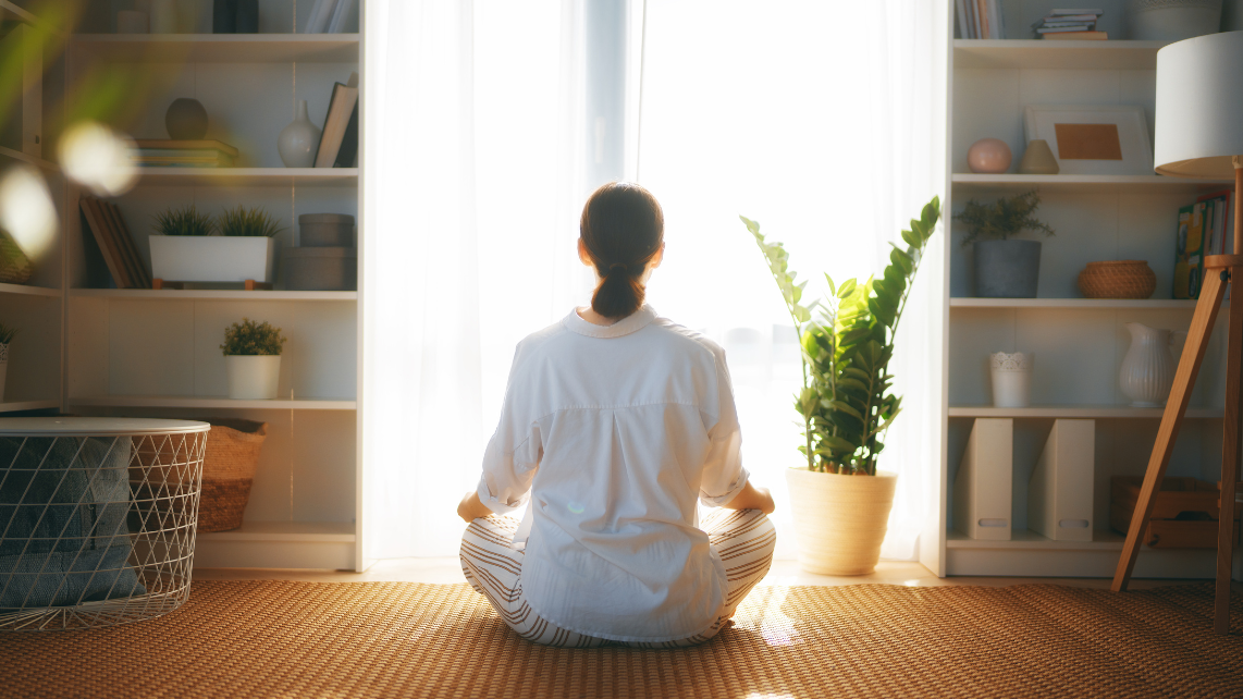 A woman meditating in her room while facing window at home