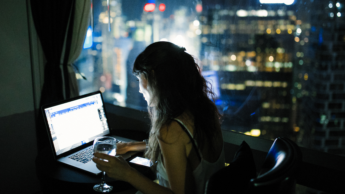 A woman sitting by the window with city view while working on her laptop