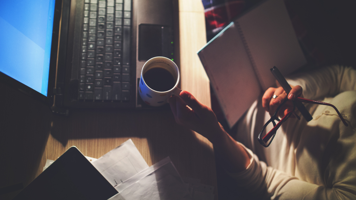A woman holding a cup of coffee while working on her laptop
