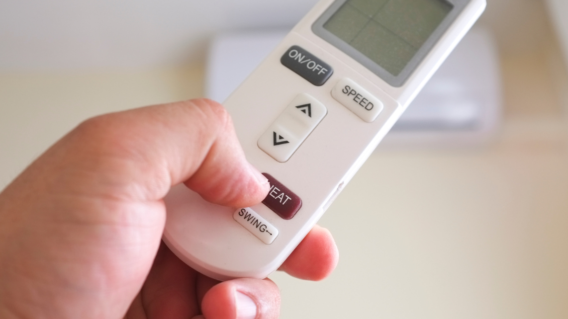 A hand with remote control pressing the Heat button