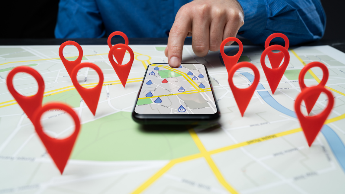 An image of a man touching his phone that is on a maps application, with a 3D maps in front of him