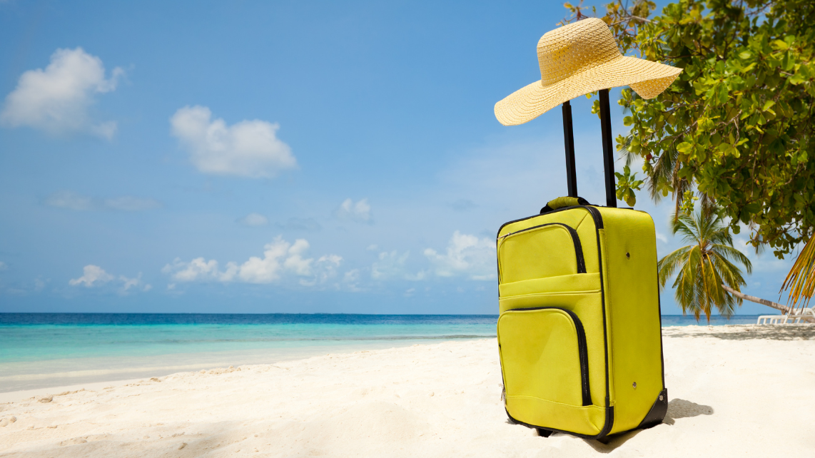 Suitcase and big straw hat on the beautiful beach