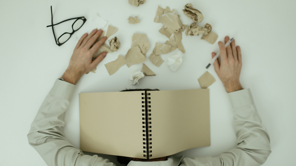 A man resting on a table with a notebook above his head